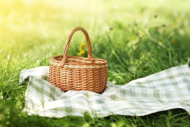 Photo of Wicker basket and blanket on green grass outdoors. Space for text