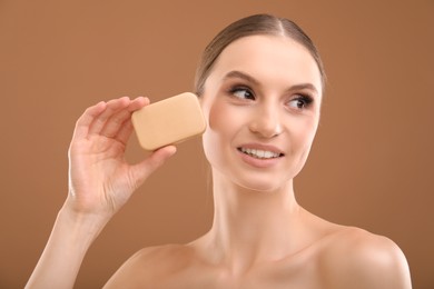 Photo of Smiling woman with soap bar on brown background, closeup