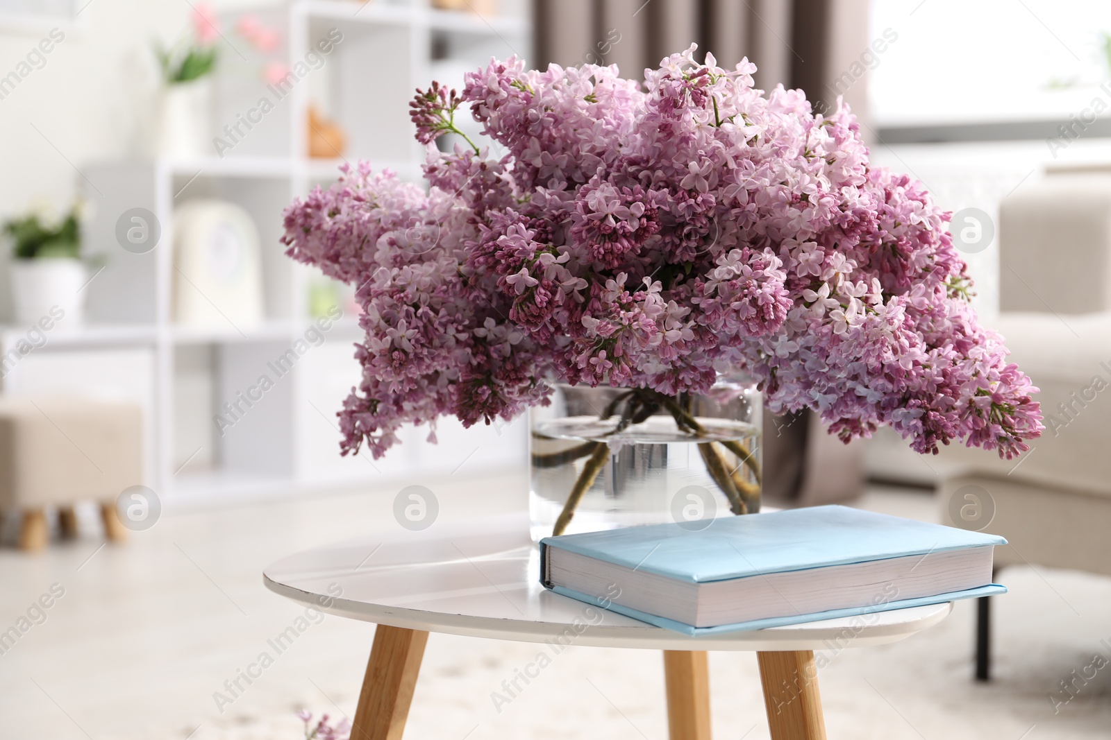 Beautiful lilac flowers in vase and book on table indoors, space for text Photo of Beautiful lilac flowers in vase and book on table indoors, space for text
