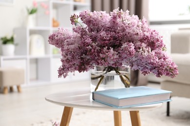 Photo of Beautiful lilac flowers in vase and book on table indoors, space for text