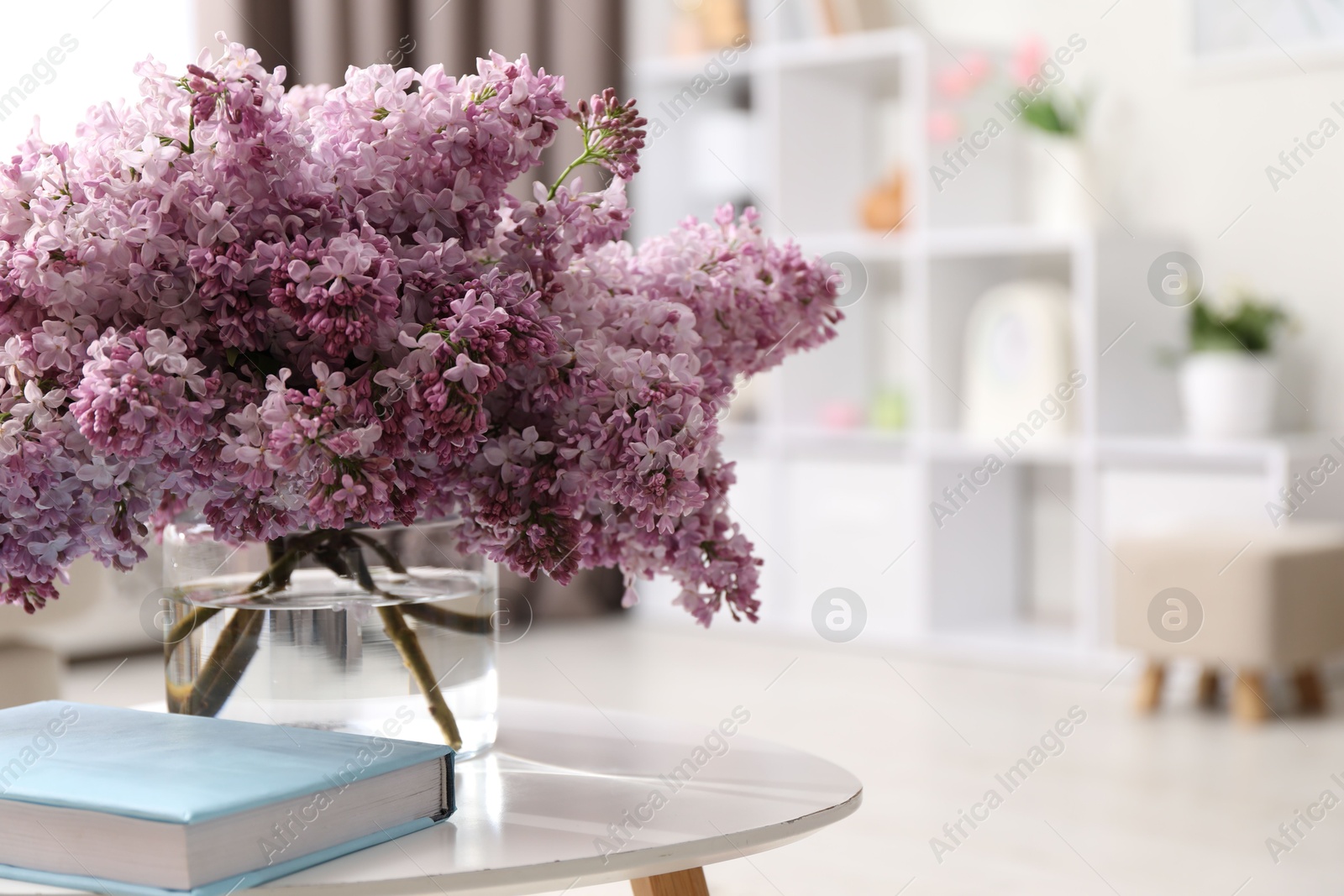 Beautiful lilac flowers in vase and book on table indoors, space for text Photo of Beautiful lilac flowers in vase and book on table indoors, space for text