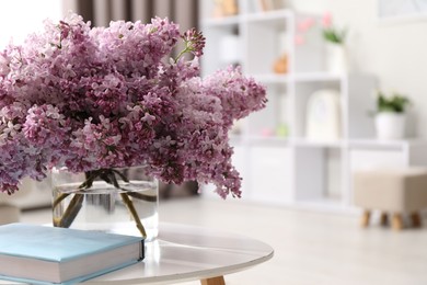Photo of Beautiful lilac flowers in vase and book on table indoors, space for text