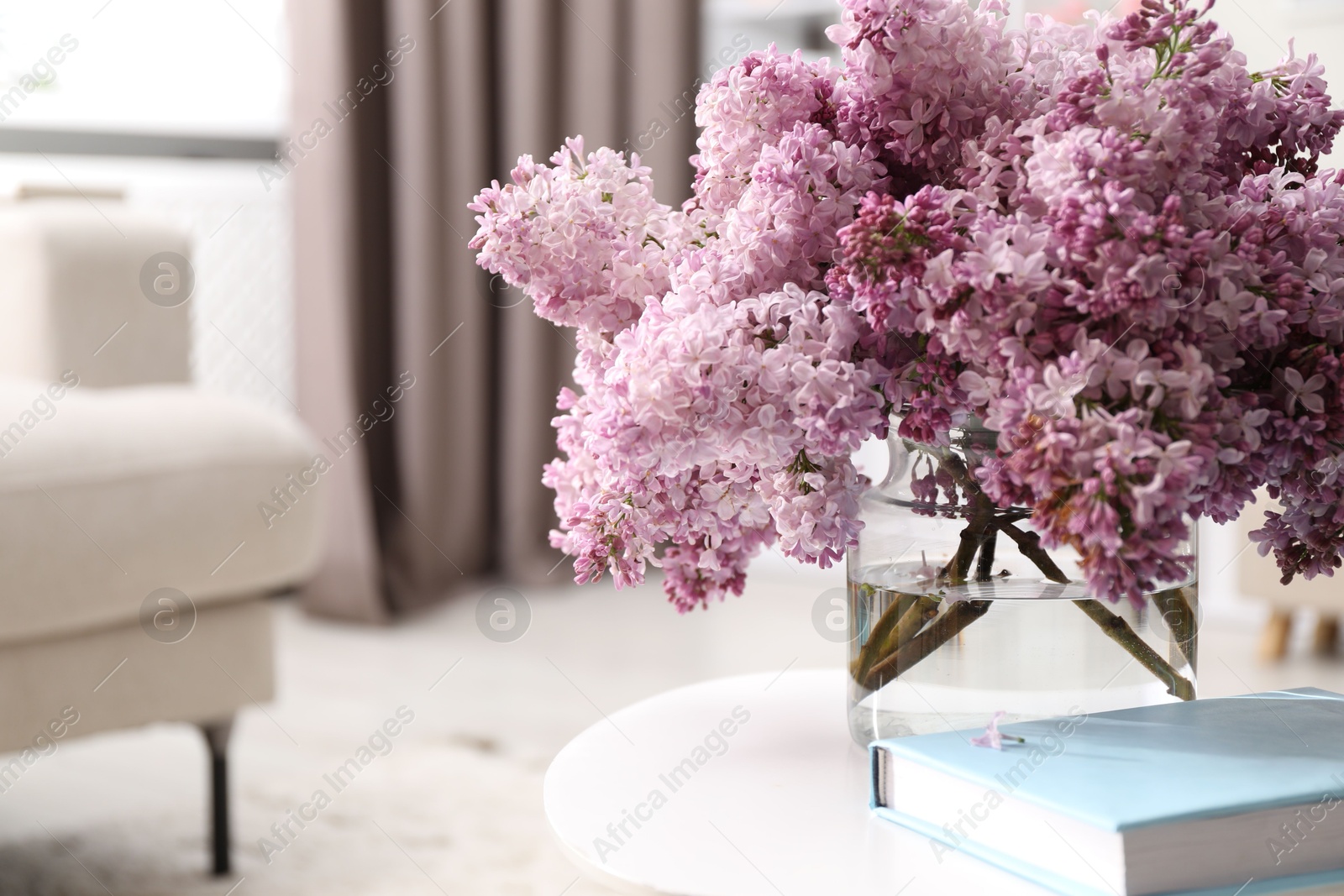 Beautiful lilac flowers in vase and book on table indoors, space for text Photo of Beautiful lilac flowers in vase and book on table indoors, space for text
