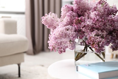 Photo of Beautiful lilac flowers in vase and book on table indoors, space for text