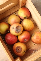 Photo of Damaged and rotten apples in wooden crate on table, top view
