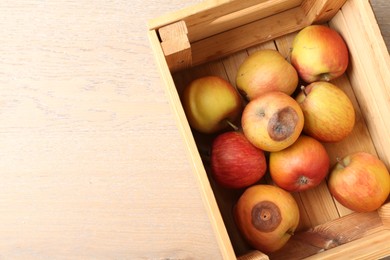 Photo of Damaged and rotten apples in wooden crate on table, top view. Space for text