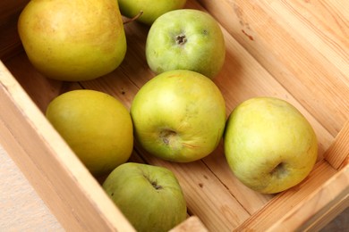 Photo of Damaged green apples in wooden crate on table, closeup