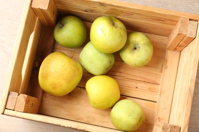 Photo of Damaged green apples in wooden crate on table, top view