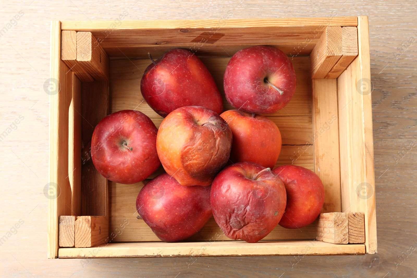 Damaged red apples in wooden crate on table, top view Photo of Damaged red apples in wooden crate on table, top view