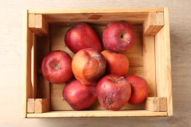 Photo of Damaged red apples in wooden crate on table, top view