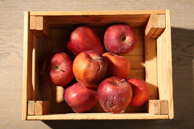 Photo of Damaged red apples in wooden crate on table, top view