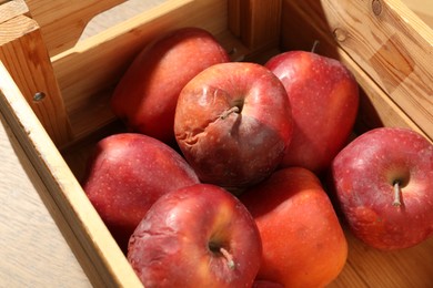 Photo of Damaged red apples in wooden crate on table, closeup
