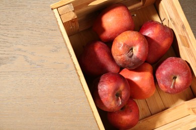 Photo of Damaged red apples in wooden crate on table, top view. Space for text