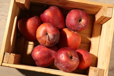 Photo of Damaged red apples in wooden crate on table, top view