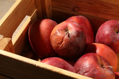 Photo of Damaged red apples in wooden crate on table, closeup