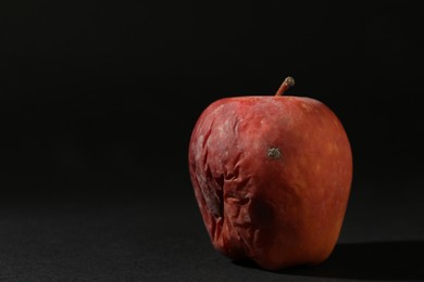 Photo of One rotten red apple on black background. Space for text