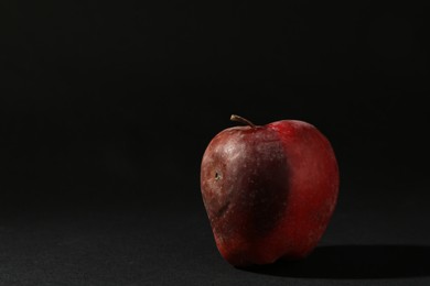 Photo of One rotten red apple on black background. Space for text