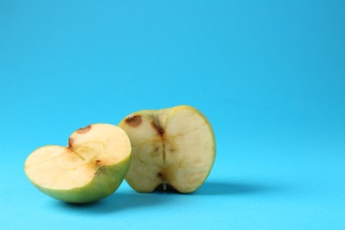 Photo of Halves of damaged apple on light blue background. Space for text