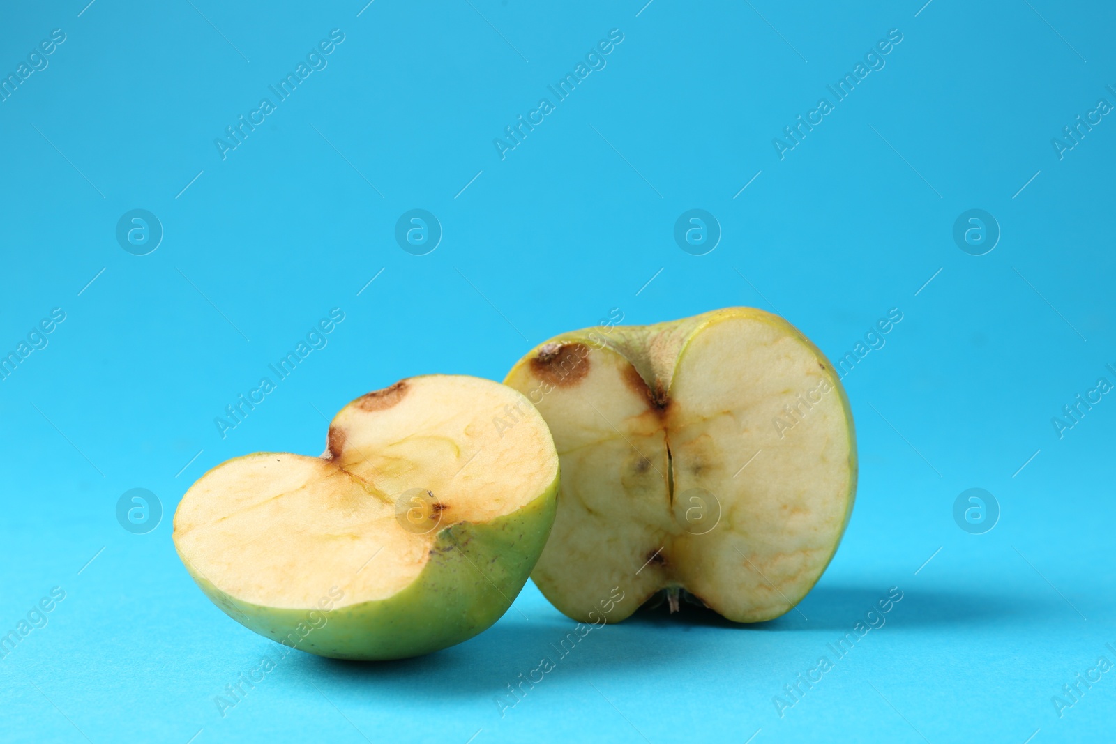 Halves of damaged apple on light blue background. Space for text Photo of Halves of damaged apple on light blue background. Space for text