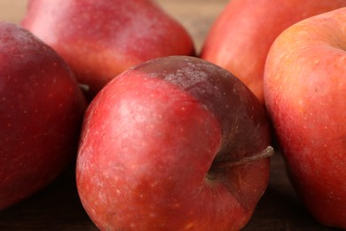 Photo of Many rotten red apples on wooden table, closeup