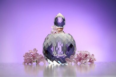 Photo of Beautiful lilac flowers and perfume on mirror surface against violet gradient background