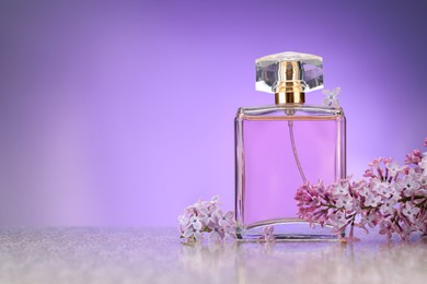 Photo of Beautiful lilac flowers and perfume on mirror surface against violet gradient background, space for text