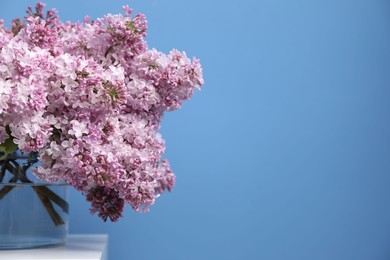 Photo of Beautiful lilac flowers in glass vase on table near light blue wall, space for text