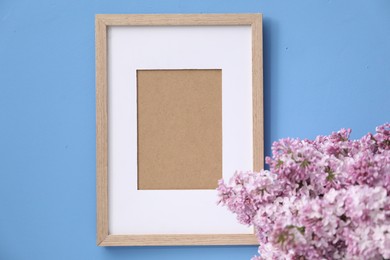 Photo of Beautiful lilac flowers and picture frame on light blue background, closeup
