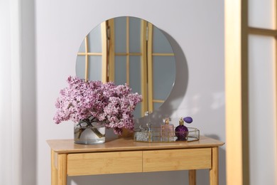 Photo of Beautiful lilac flowers in glass vase and perfumes on wooden table indoors
