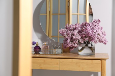 Photo of Beautiful lilac flowers in glass vase and perfumes on wooden table indoors