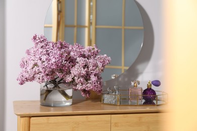 Photo of Beautiful lilac flowers in glass vase and perfumes on wooden table indoors