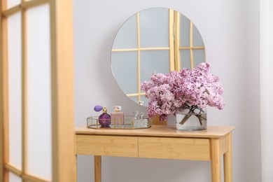 Photo of Beautiful lilac flowers in glass vase and perfumes on wooden table indoors