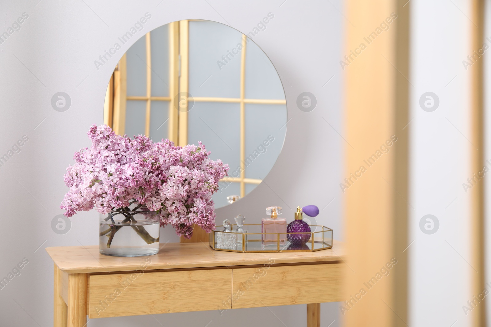 Beautiful lilac flowers in glass vase and perfumes on wooden table indoors Photo of Beautiful lilac flowers in glass vase and perfumes on wooden table indoors