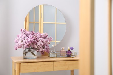 Photo of Beautiful lilac flowers in glass vase and perfumes on wooden table indoors