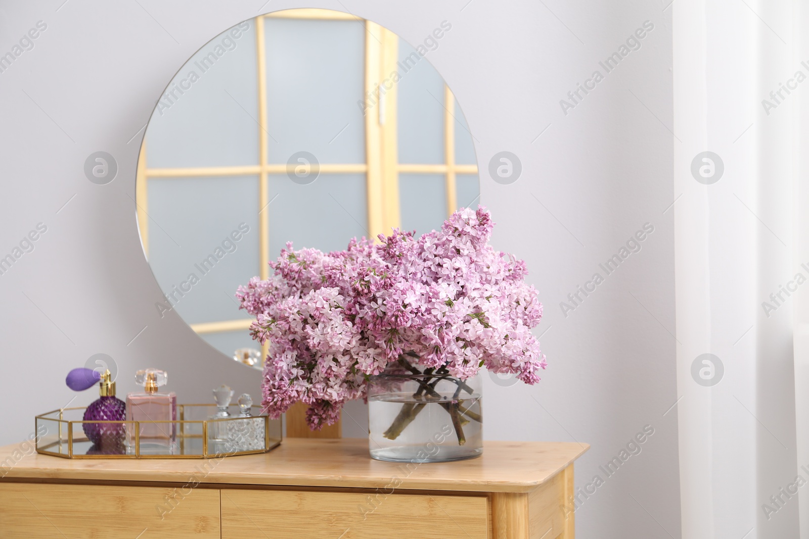 Beautiful lilac flowers in glass vase and perfumes on wooden table indoors Photo of Beautiful lilac flowers in glass vase and perfumes on wooden table indoors