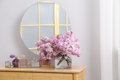 Photo of Beautiful lilac flowers in glass vase and perfumes on wooden table indoors
