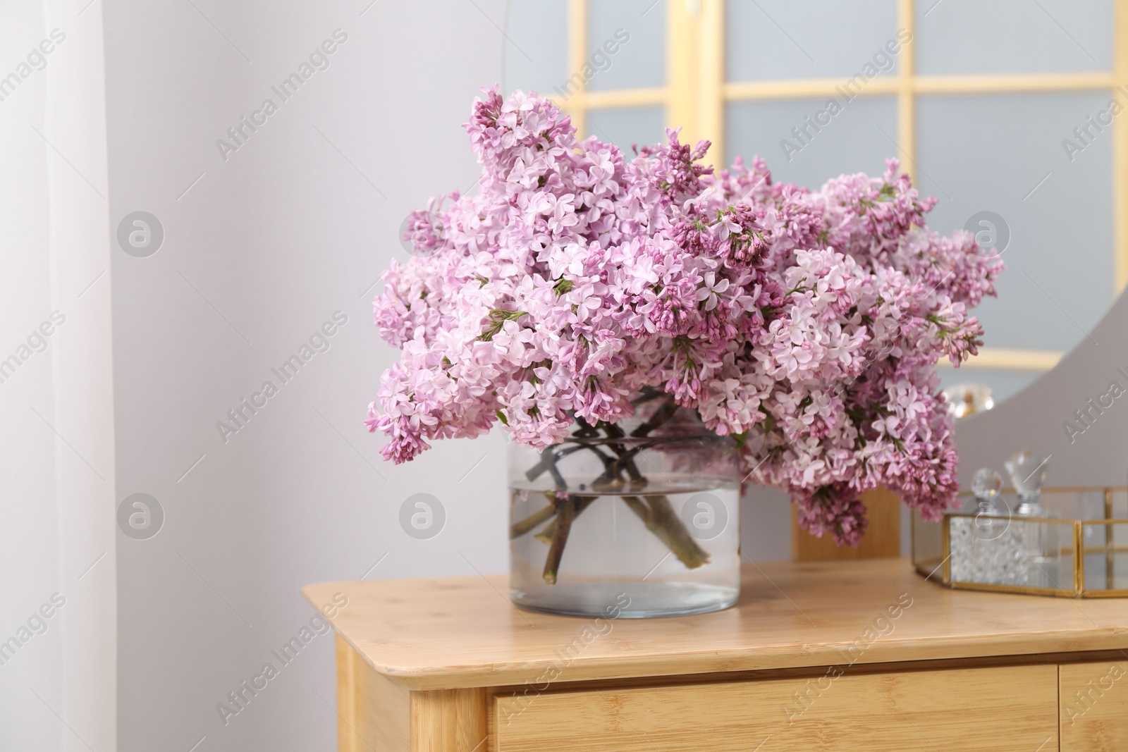Beautiful lilac flowers in glass vase and perfumes on wooden table indoors, space for text Photo of Beautiful lilac flowers in glass vase and perfumes on wooden table indoors, space for text