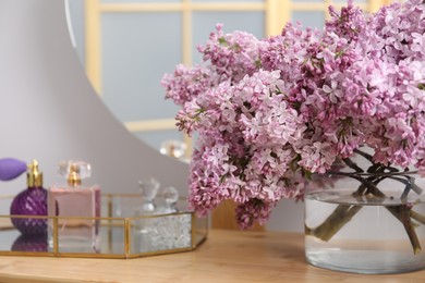 Photo of Beautiful lilac flowers in glass vase and perfumes on wooden table indoors, closeup