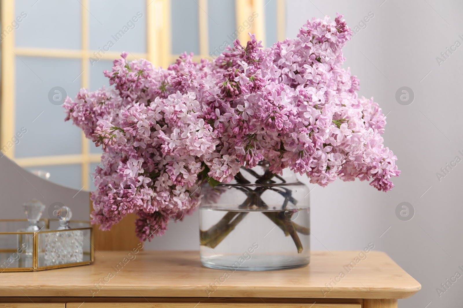 Beautiful lilac flowers in glass vase and perfumes on wooden table indoors Photo of Beautiful lilac flowers in glass vase and perfumes on wooden table indoors