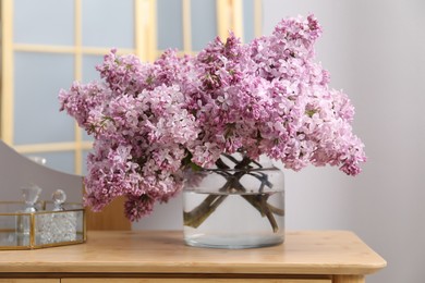 Photo of Beautiful lilac flowers in glass vase and perfumes on wooden table indoors