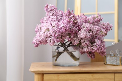 Photo of Beautiful lilac flowers in glass vase and perfumes on wooden table indoors
