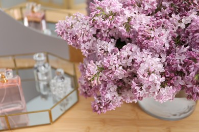 Photo of Beautiful lilac flowers in glass vase and perfumes on wooden table indoors, closeup