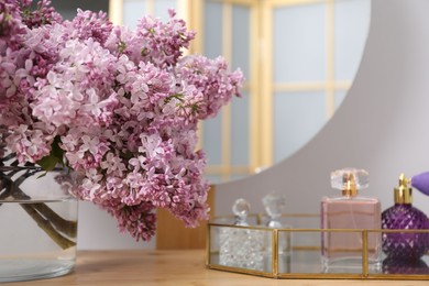 Photo of Beautiful lilac flowers in glass vase and perfumes on wooden table indoors, closeup