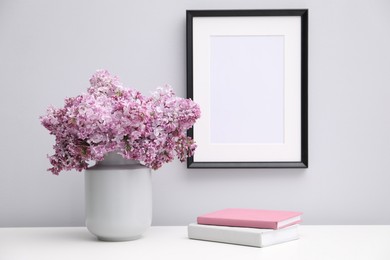 Photo of Beautiful lilac flowers in vase, books and picture frame indoors