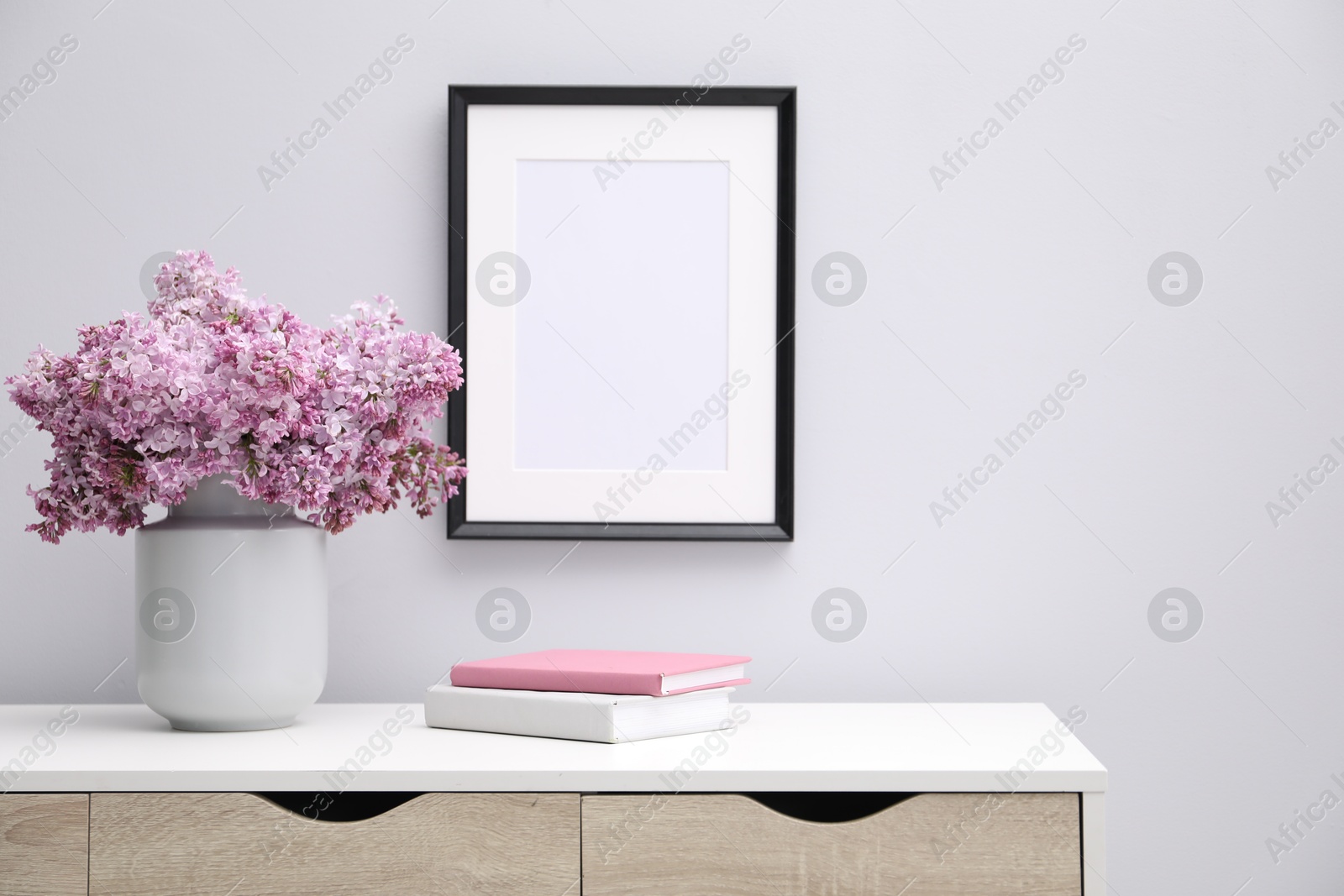 Beautiful lilac flowers in vase, books and picture frame indoors Photo of Beautiful lilac flowers in vase, books and picture frame indoors
