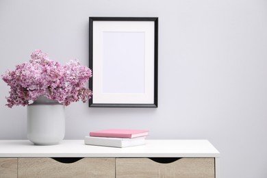 Photo of Beautiful lilac flowers in vase, books and picture frame indoors