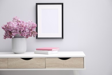 Photo of Beautiful lilac flowers in vase, books and picture frame indoors