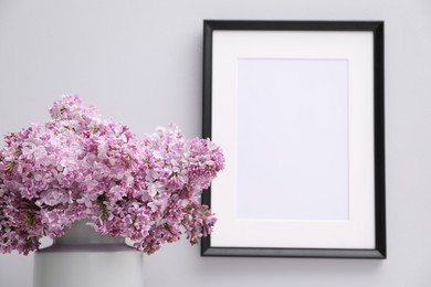Photo of Beautiful lilac flowers in vase and picture frame on white background, closeup