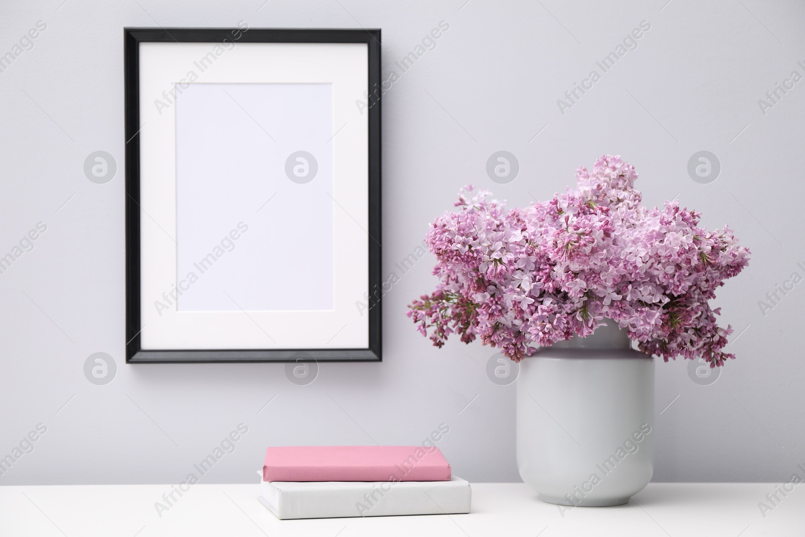 Beautiful lilac flowers in vase, books and picture frame indoors Photo of Beautiful lilac flowers in vase, books and picture frame indoors