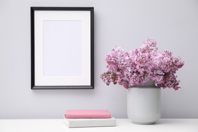 Photo of Beautiful lilac flowers in vase, books and picture frame indoors
